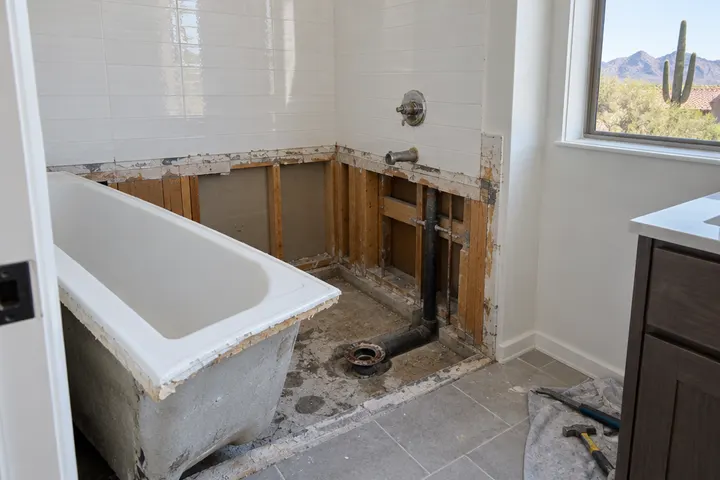 Bathtub being removed from an alcove during a remodel, wall tile cut away, drain exposed
